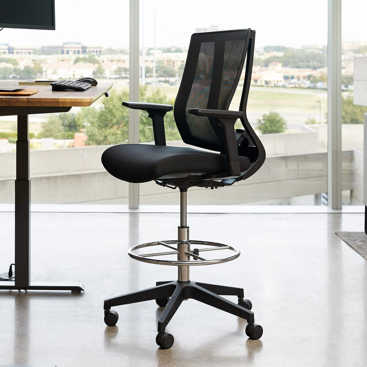 Vari Drafting Chair 401495 black mesh-back chair with adjustable arms and foot ring beside a standing desk